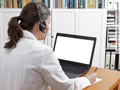 Eine Ärztin sitzt mit Headset vor einem Laptop und führt eine Tele-Sprechstunde durch. 