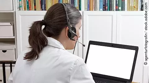 Eine Ärztin sitzt mit Headset vor einem Laptop und führt eine Tele-Sprechstunde durch. 