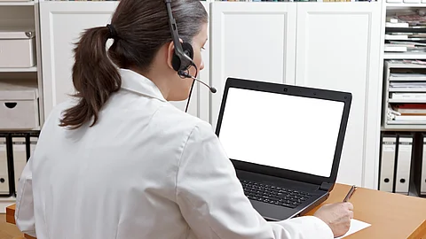 Videosprechstunde Eine Ärztin sitzt mit Headset vor einem Laptop und führt eine Tele-Sprechstunde durch.