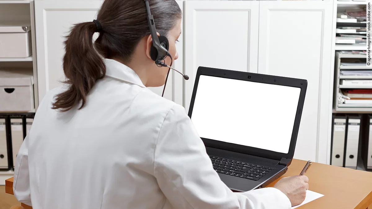Videosprechstunde Eine Ärztin sitzt mit Headset vor einem Laptop und führt eine Tele-Sprechstunde durch.