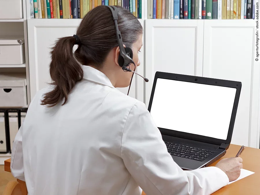 Videosprechstunde Eine Ärztin sitzt mit Headset vor einem Laptop und führt eine Tele-Sprechstunde durch.
