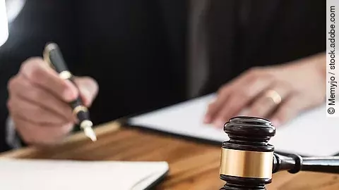 Rechtsspruch Ein Richterhammer liegt auf einem Tisch. Hinter im ist verschwommen ein Mann in Richterrobe zu sehen.