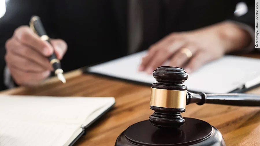 Rechtsspruch Ein Richterhammer liegt auf einem Tisch. Hinter im ist verschwommen ein Mann in Richterrobe zu sehen.