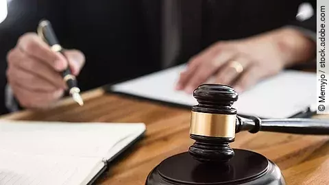 Rechtsspruch Ein Richterhammer liegt auf einem Tisch. Hinter im ist verschwommen ein Mann in Richterrobe zu sehen.