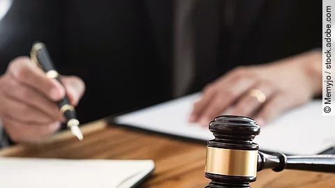 Rechtsspruch Ein Richterhammer liegt auf einem Tisch. Hinter im ist verschwommen ein Mann in Richterrobe zu sehen.