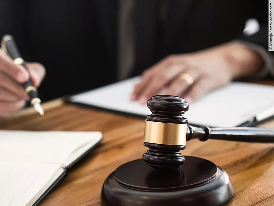 Rechtsspruch Ein Richterhammer liegt auf einem Tisch. Hinter im ist verschwommen ein Mann in Richterrobe zu sehen.