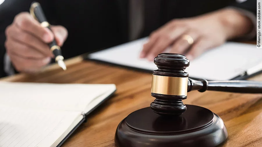 Rechtsspruch Ein Richterhammer liegt auf einem Tisch. Hinter im ist verschwommen ein Mann in Richterrobe zu sehen.