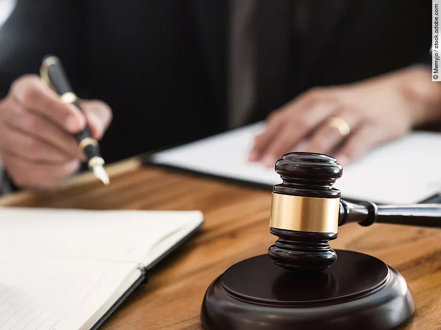 Rechtsspruch Ein Richterhammer liegt auf einem Tisch. Hinter im ist verschwommen ein Mann in Richterrobe zu sehen.