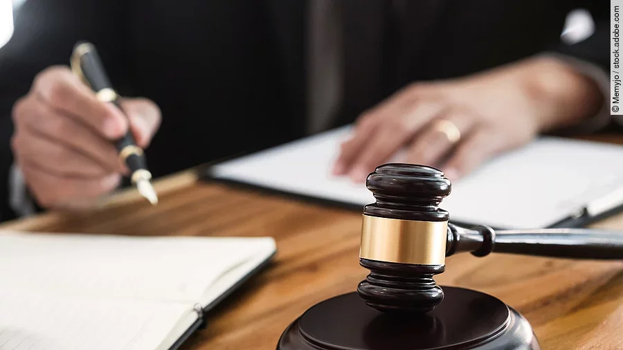 Rechtsspruch Ein Richterhammer liegt auf einem Tisch. Hinter im ist verschwommen ein Mann in Richterrobe zu sehen.