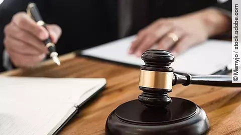 Rechtsspruch Ein Richterhammer liegt auf einem Tisch. Hinter im ist verschwommen ein Mann in Richterrobe zu sehen.