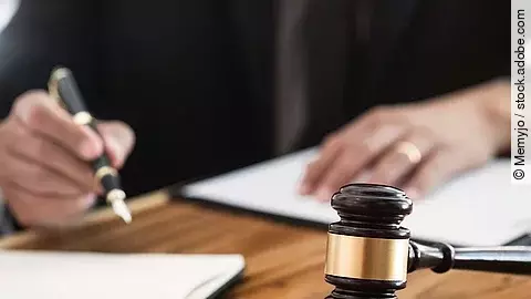 Rechtsspruch Ein Richterhammer liegt auf einem Tisch. Hinter im ist verschwommen ein Mann in Richterrobe zu sehen.