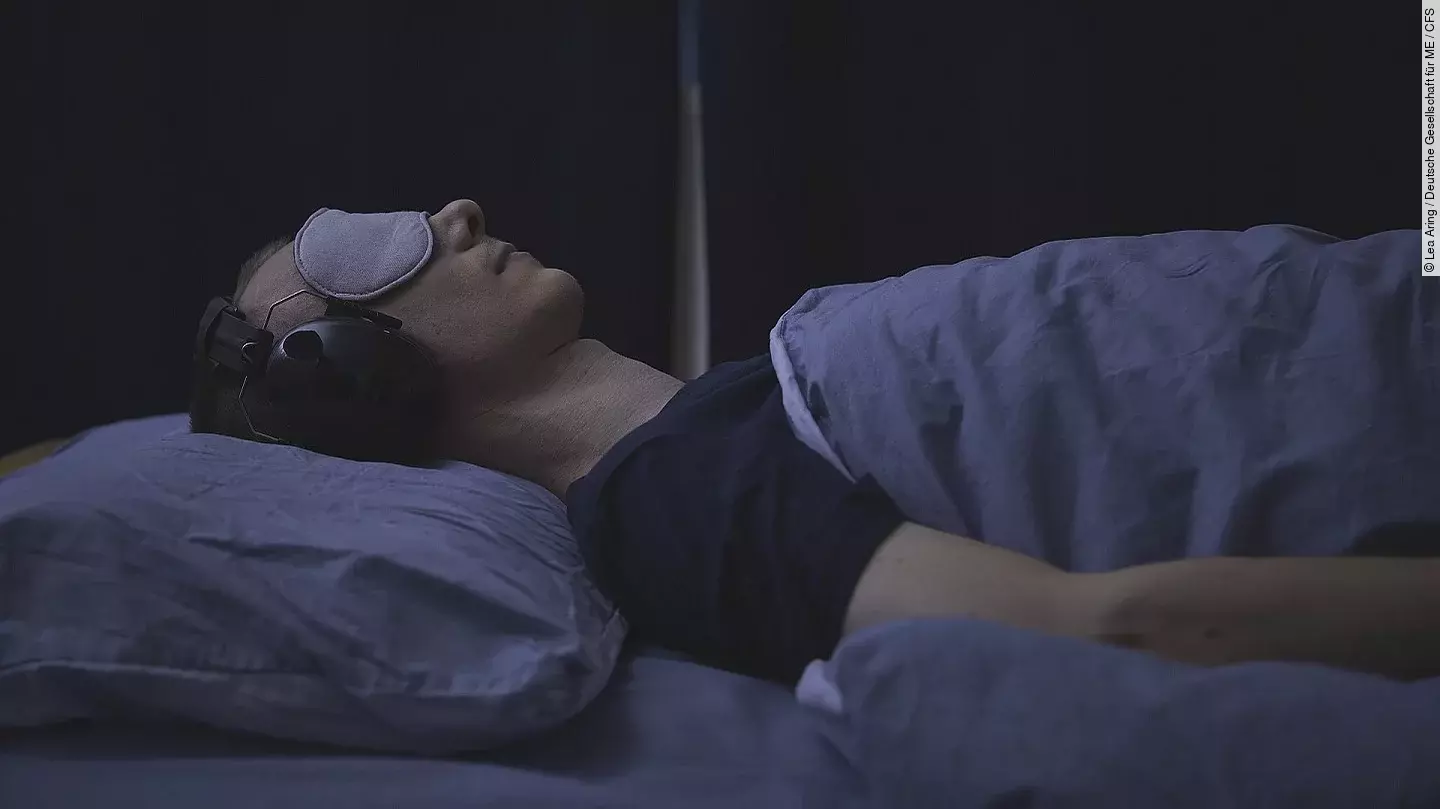 Frau mit Schlafmaske und Kopfhörern im abgedunkelten Zimmer.