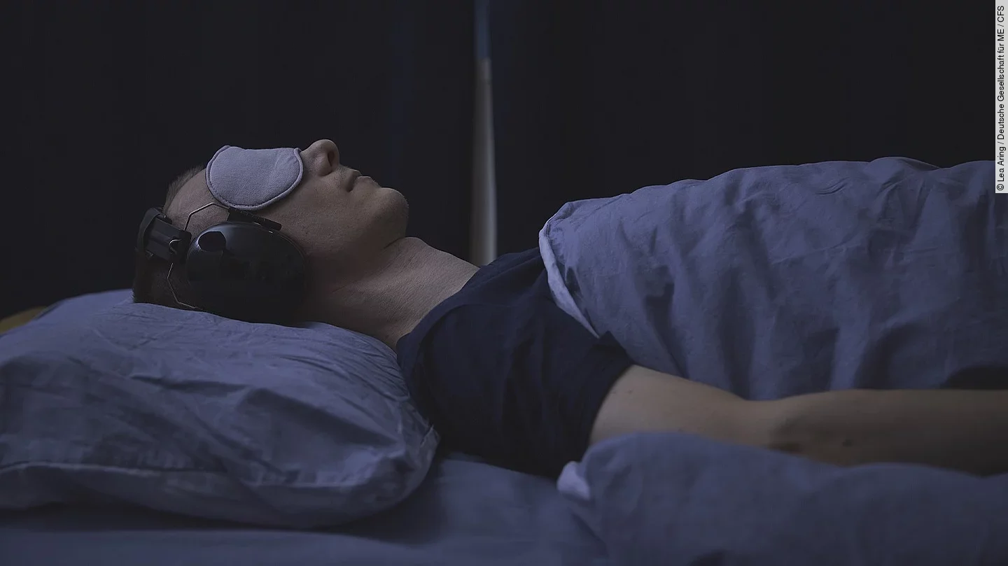 Frau mit Schlafmaske und Kopfhörern im abgedunkelten Zimmer.