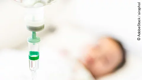 Eine Infusion, im Hintergrund ist verschwommen ein Patient zu sehen