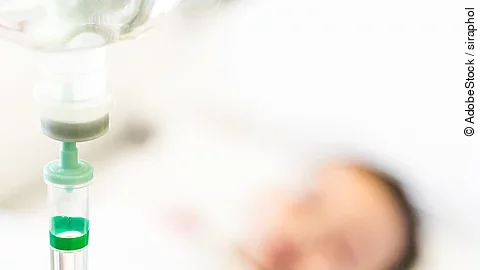 Patient mit Infusion Eine Infusion, im Hintergrund ist verschwommen ein Patient zu sehen