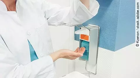 Ein Arzt betätigt mit dem Ellenbogen einen Desinfektionsspender im Krankenhaus.
