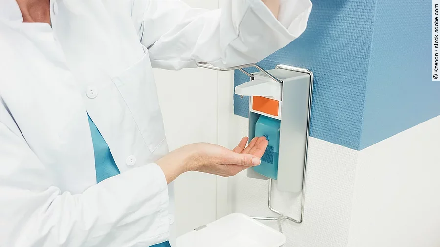 Ein Arzt betätigt mit dem Ellenbogen einen Desinfektionsspender im Krankenhaus.