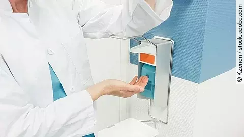 Ein Arzt betätigt mit dem Ellenbogen einen Desinfektionsspender im Krankenhaus.