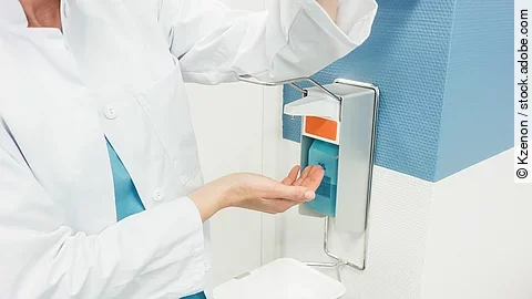 Ein Arzt betätigt mit dem Ellenbogen einen Desinfektionsspender im Krankenhaus.
