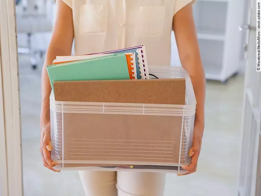 Der Torso einer Frau: Sie hält einen Pappkarton mit einigen Dokumenten darin.