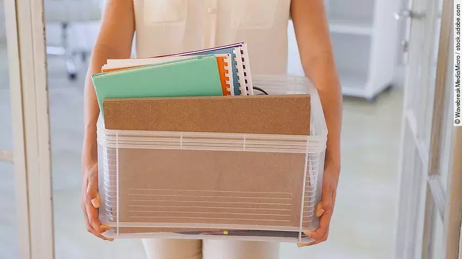 Der Torso einer Frau: Sie hält einen Pappkarton mit einigen Dokumenten darin.