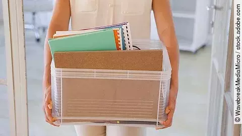 Der Torso einer Frau: Sie hält einen Pappkarton mit einigen Dokumenten darin.