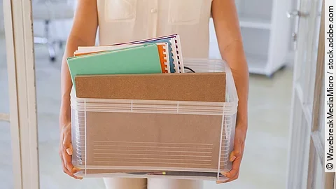 Der Torso einer Frau: Sie hält einen Pappkarton mit einigen Dokumenten darin.