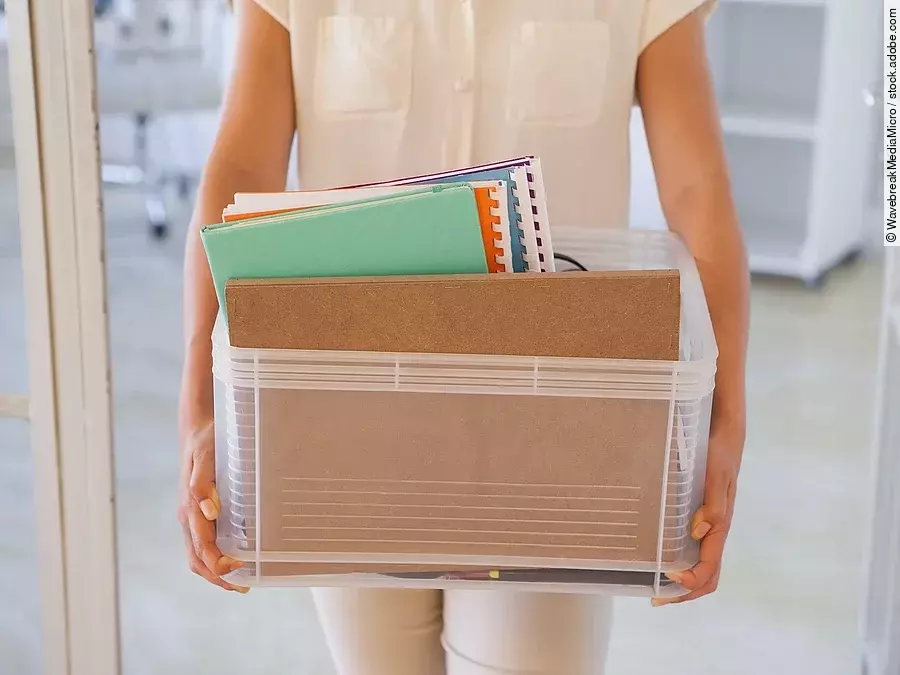 Der Torso einer Frau: Sie hält einen Pappkarton mit einigen Dokumenten darin.