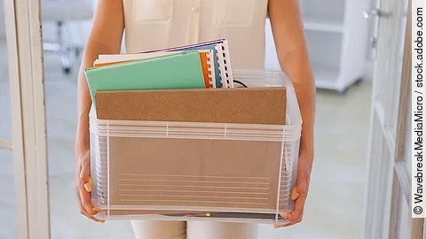 Der Torso einer Frau: Sie hält einen Pappkarton mit einigen Dokumenten darin.