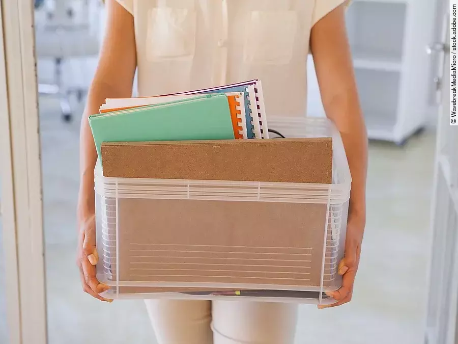 Der Torso einer Frau: Sie hält einen Pappkarton mit einigen Dokumenten darin.
