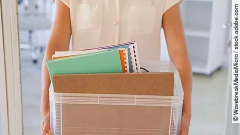 Der Torso einer Frau: Sie hält einen Pappkarton mit einigen Dokumenten darin.