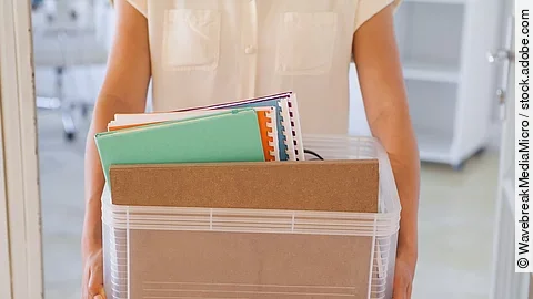 Der Torso einer Frau: Sie hält einen Pappkarton mit einigen Dokumenten darin.
