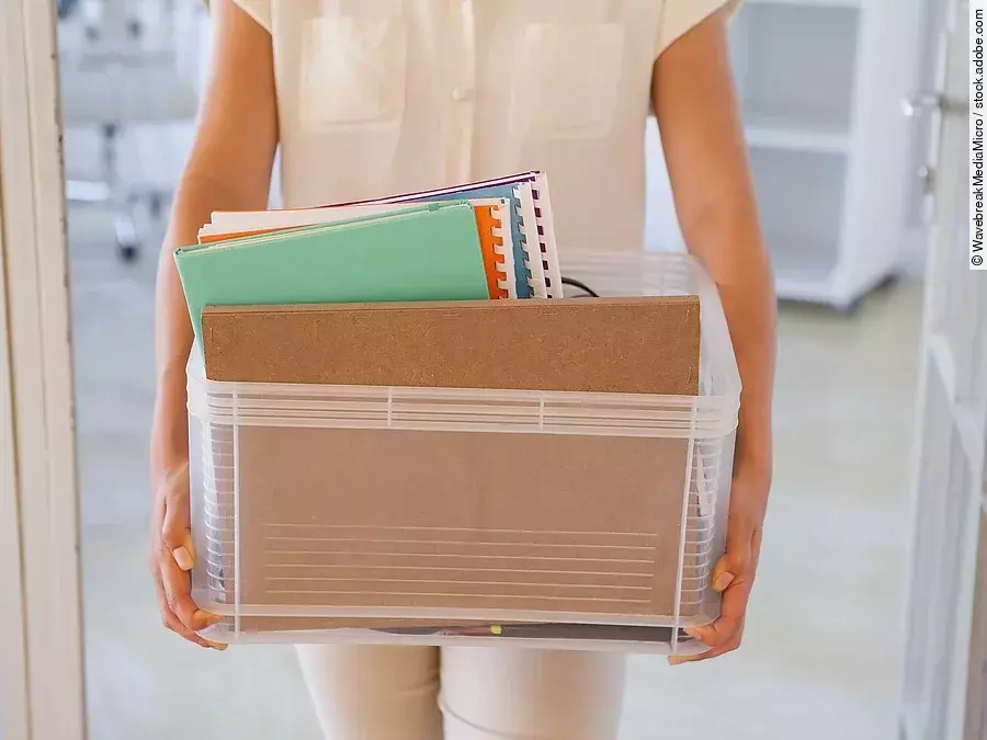 Der Torso einer Frau: Sie hält einen Pappkarton mit einigen Dokumenten darin.