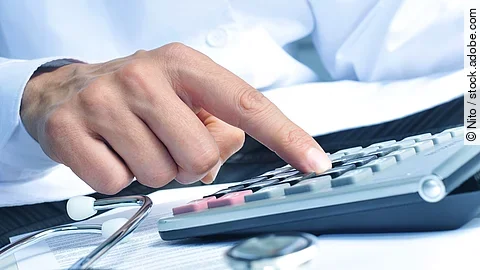 Taschenrechner Die Hand eines Mannes in blauem Hemd tippt auf einem Taschenrechner. Daneben liegt ein Stethoskop.