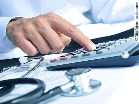 Taschenrechner Die Hand eines Mannes in blauem Hemd tippt auf einem Taschenrechner. Daneben liegt ein Stethoskop.