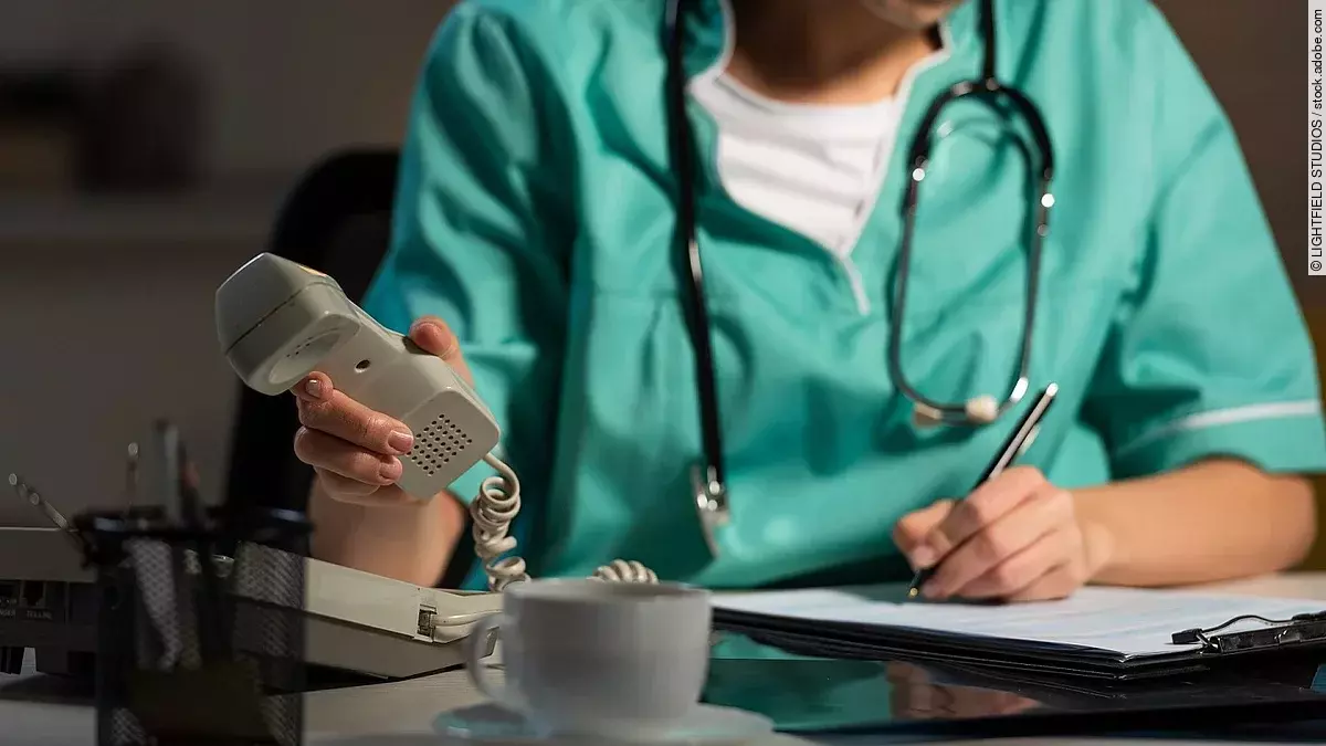Ärztin sitzt am Schreibtisch und hebt den Telefonhörer ab.
