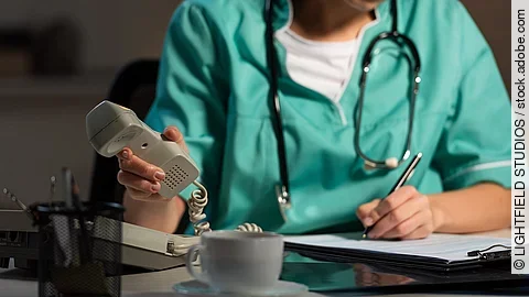 Ärztin am Schreibtisch Ärztin sitzt am Schreibtisch und hebt den Telefonhörer ab.