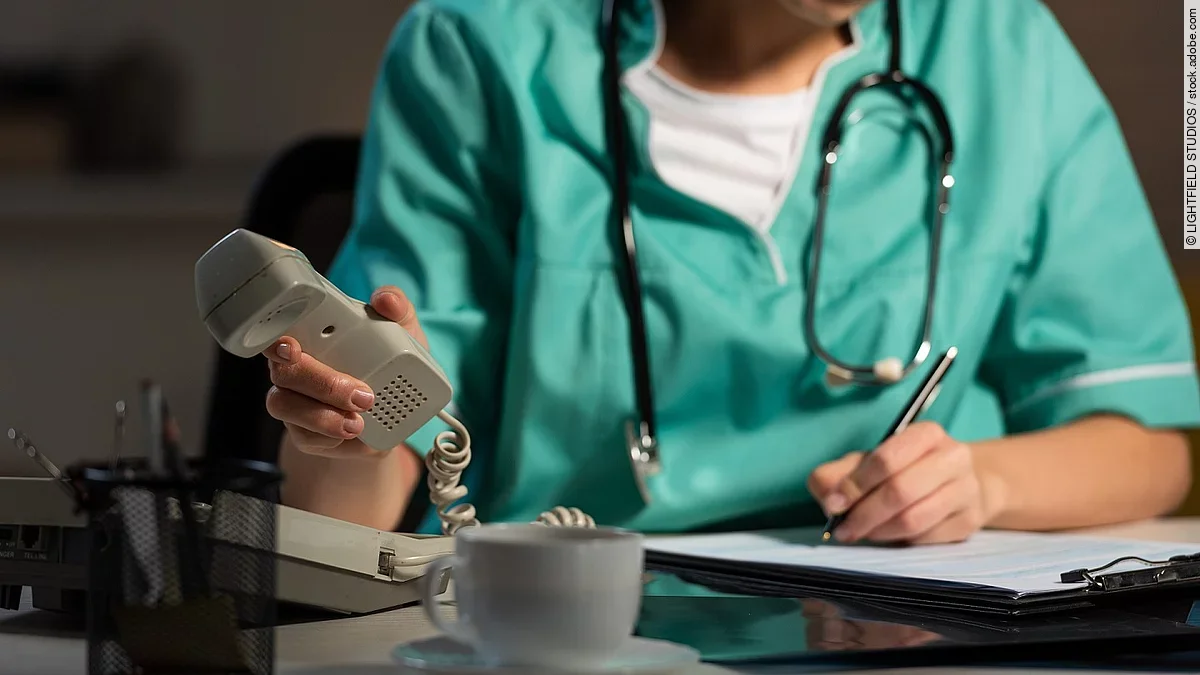 Ärztin am Schreibtisch Ärztin sitzt am Schreibtisch und hebt den Telefonhörer ab.