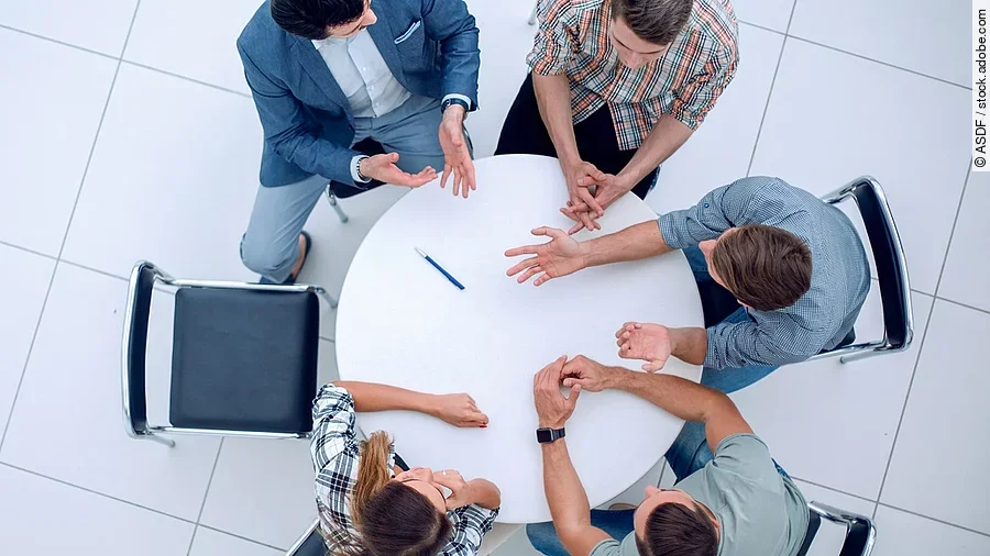 Gesprächsrunde Personen sitzen an einem kleinen runden Tisch und diskutieren. Ein Sitzplatz ist frei.