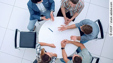 Gesprächsrunde Personen sitzen an einem kleinen runden Tisch und diskutieren. Ein Sitzplatz ist frei.