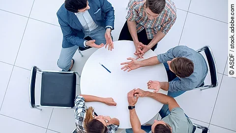 Personen sitzen an einem kleinen runden Tisch und diskutieren. Ein Sitzplatz ist frei.