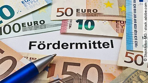Euro-Scheine umgeben einen Zettel mit der Aufschrift "Fördermittel"
