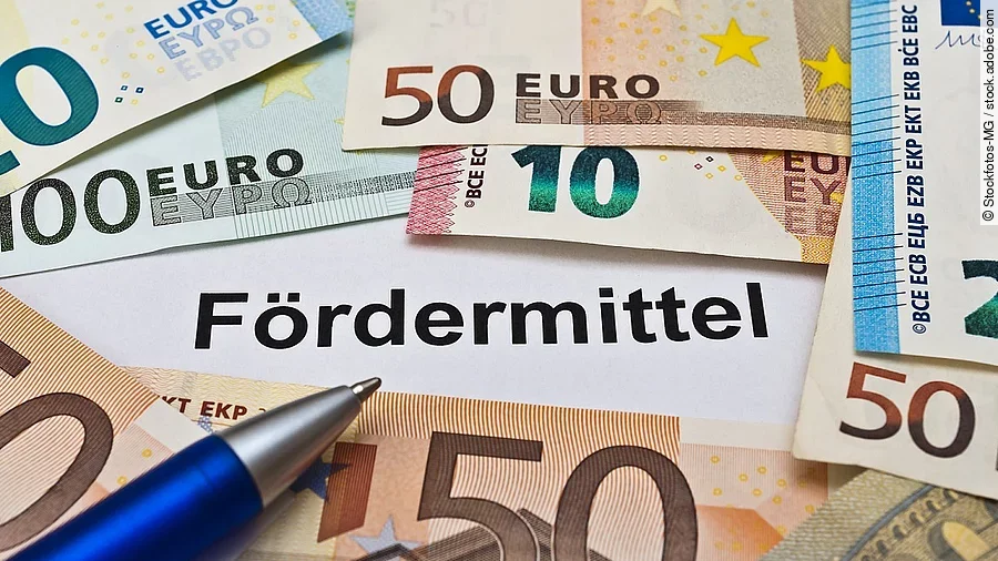 Euro-Scheine umgeben einen Zettel mit der Aufschrift "Fördermittel"