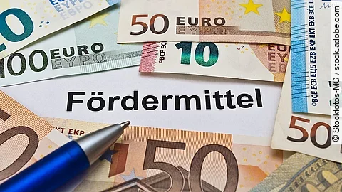 Euro-Scheine umgeben einen Zettel mit der Aufschrift "Fördermittel"
