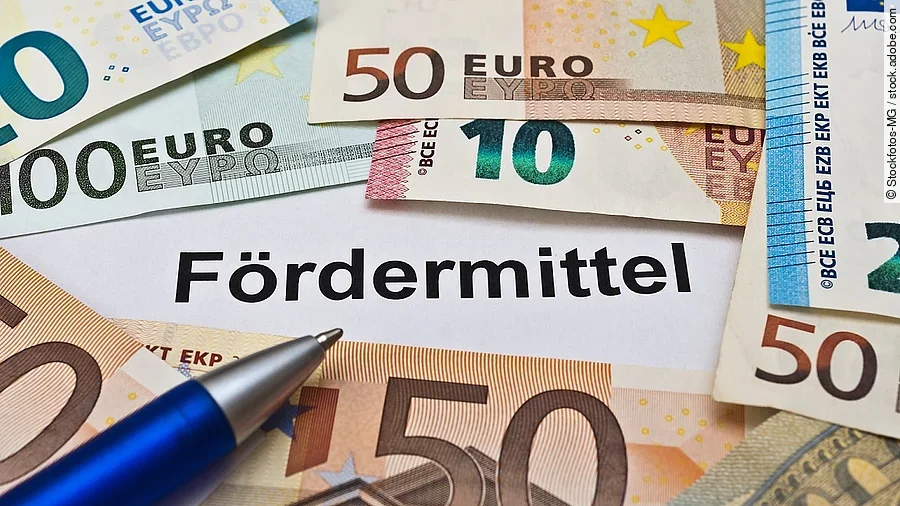 Euro-Scheine umgeben einen Zettel mit der Aufschrift "Fördermittel"