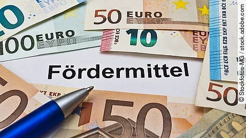 Euro-Scheine umgeben einen Zettel mit der Aufschrift "Fördermittel"