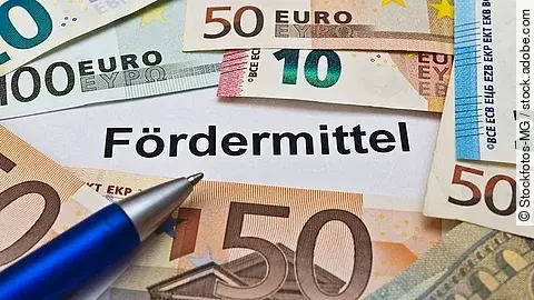 Euro-Scheine umgeben einen Zettel mit der Aufschrift "Fördermittel"