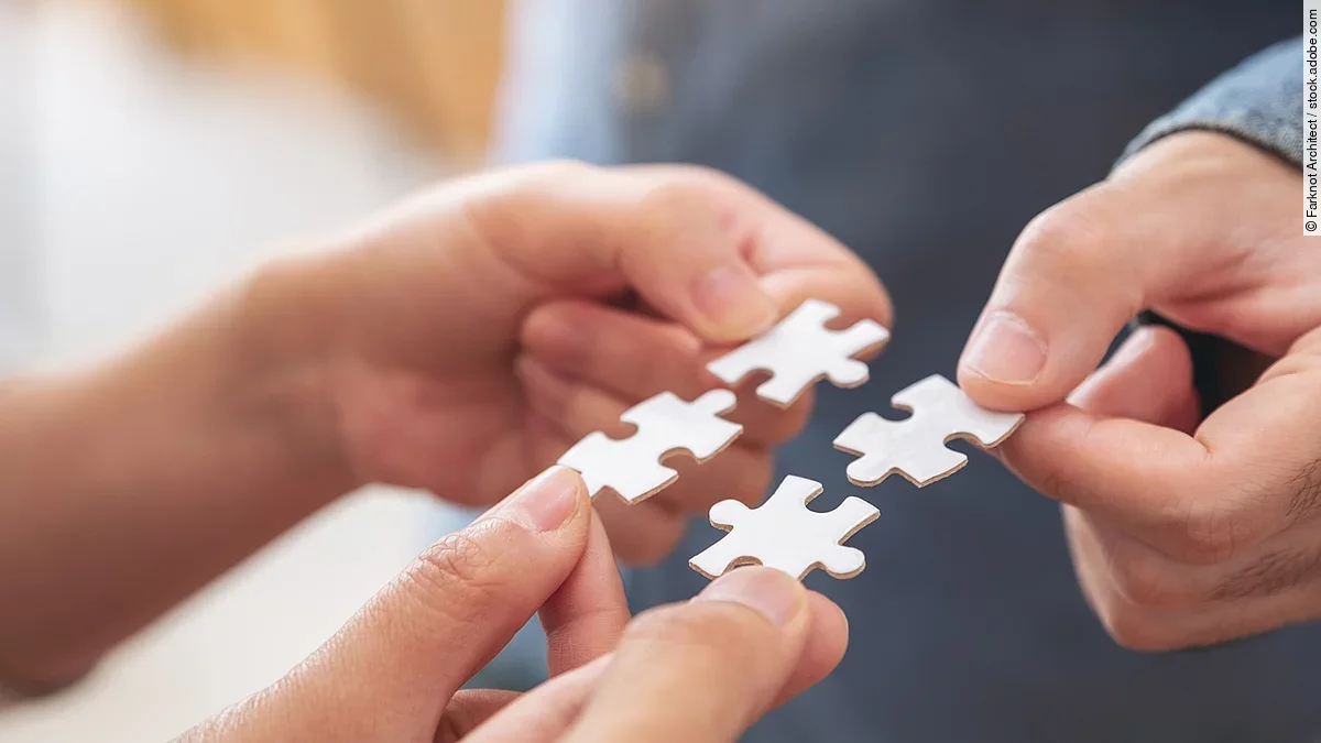 Vier Hände halten jeweils ein weißes Puzzleteil und setzen sie zusammen.