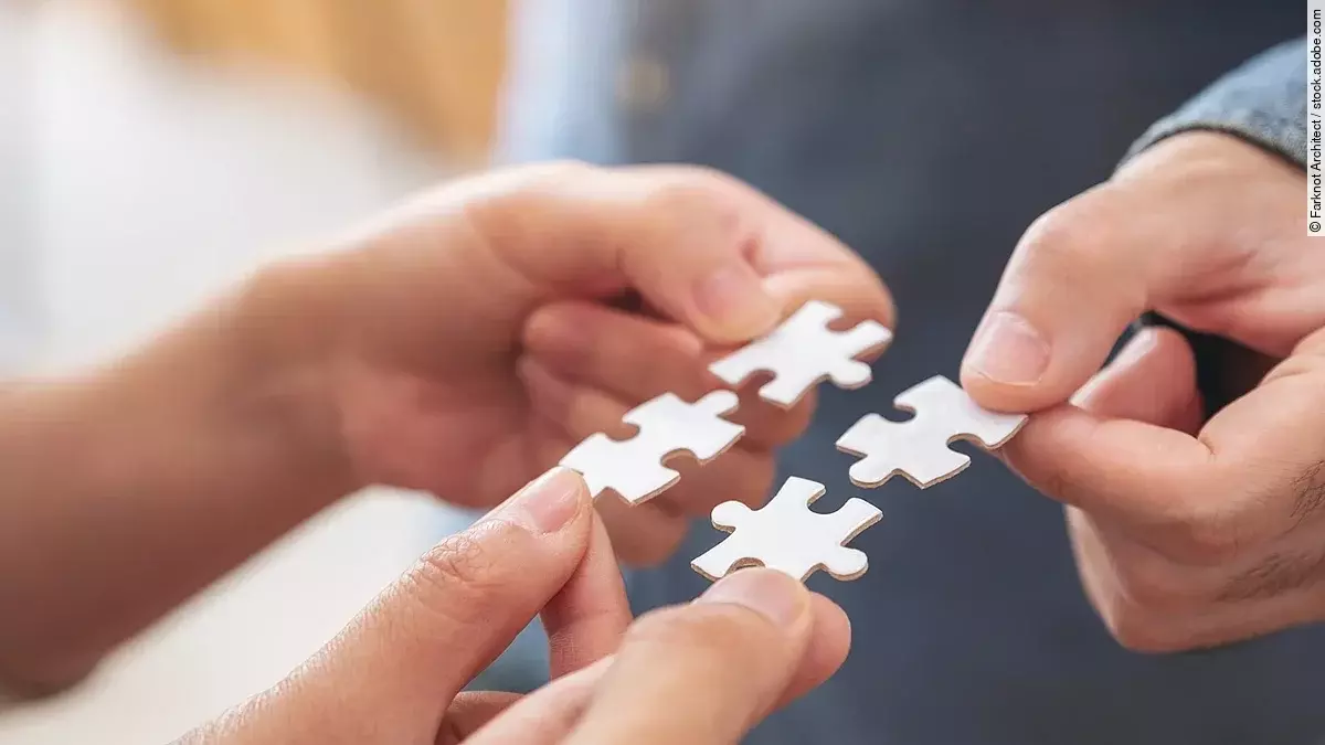 Vier Hände halten jeweils ein weißes Puzzleteil und setzen sie zusammen.