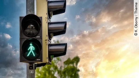 Ampel Fußgängerampel zeigt grünes Ampelmännchen. Im Hintergrund scheint die Sonne.